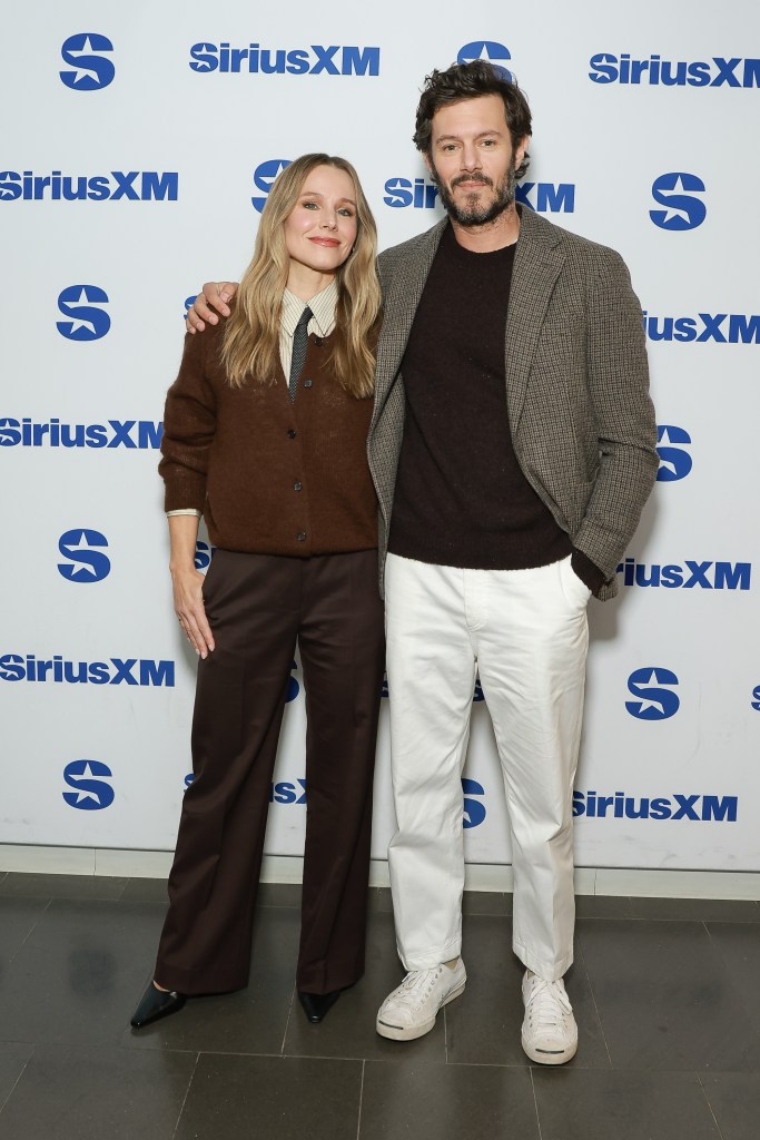 Kristen Bell and Adam Brody pose in front of a white SiriusXM branded backdrop.