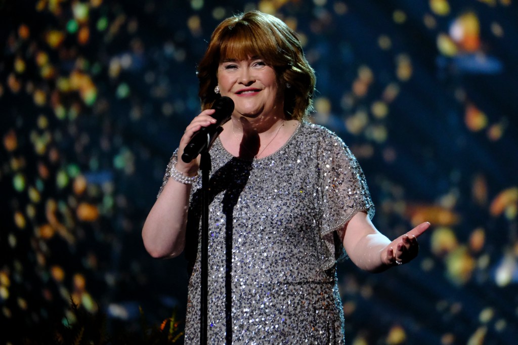 Susan Boyle smiling and holding a microphone at an America's Got Talent show.