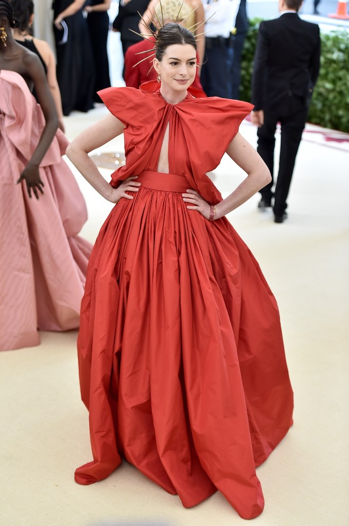 Anne Hathaway in a red gown at the Met Gala, complemented by a golden headpiece.